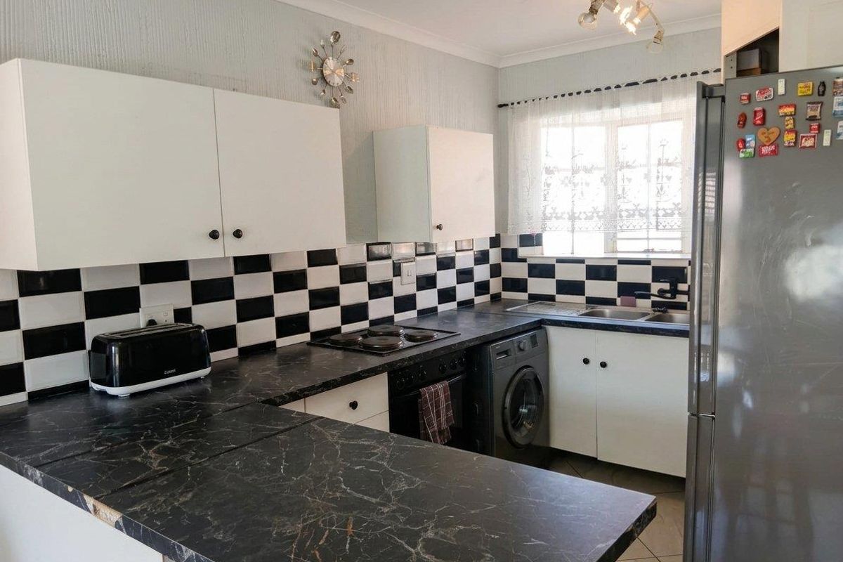 A functional kitchen featuring black marble-effect laminate countertops, a checkerboard tile backsplash, built-in cabinetry, and integrated cooking appliances.