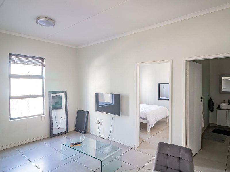 A bright living area featuring tiled flooring and neutral walls, with direct access to an adjoining bedroom and bathroom.