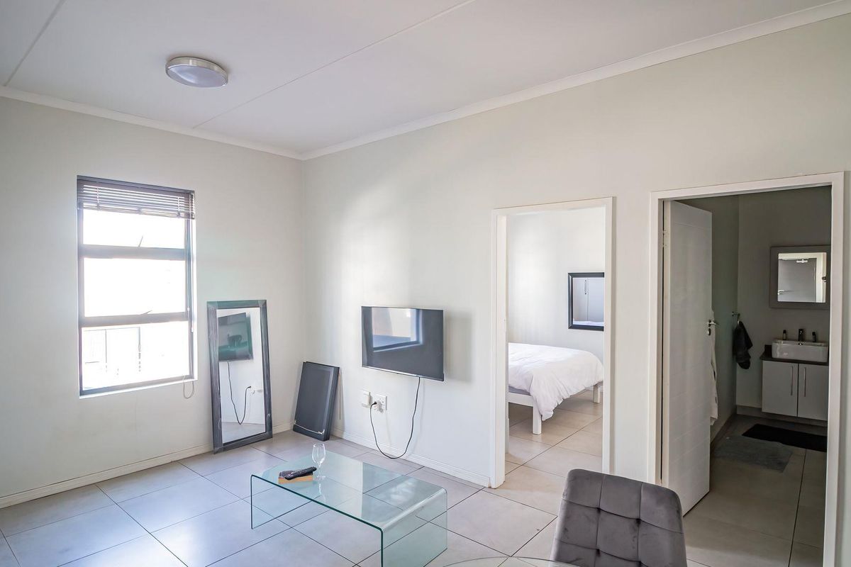 A bright living area featuring tiled flooring and neutral walls, with direct access to an adjoining bedroom and bathroom.