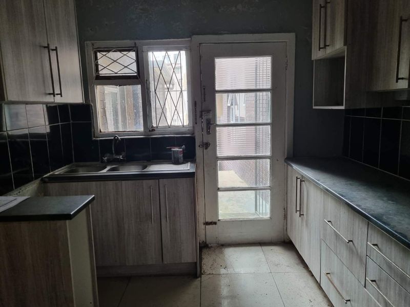 A dated kitchen featuring laminate cabinetry, tiled flooring, and direct access to an exterior area, requiring cosmetic updates and refurbishment.