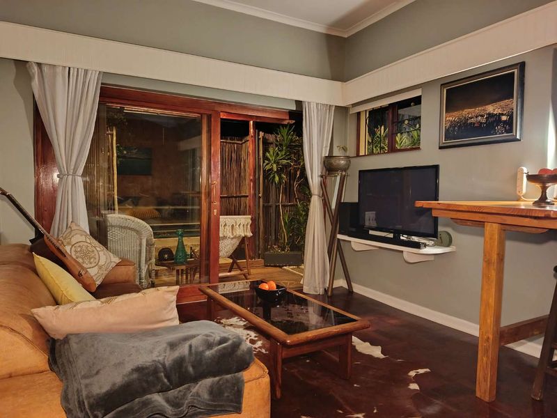 A cozy living room featuring dark wooden flooring, a built-in wall shelf, and large sliding glass doors that open to an outdoor patio area.