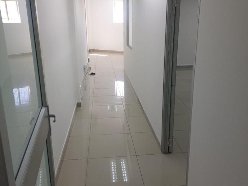 A clean, well-lit office hallway featuring polished tile flooring, suspended ceilings with recessed lighting, and modern aluminium-framed glass doors.