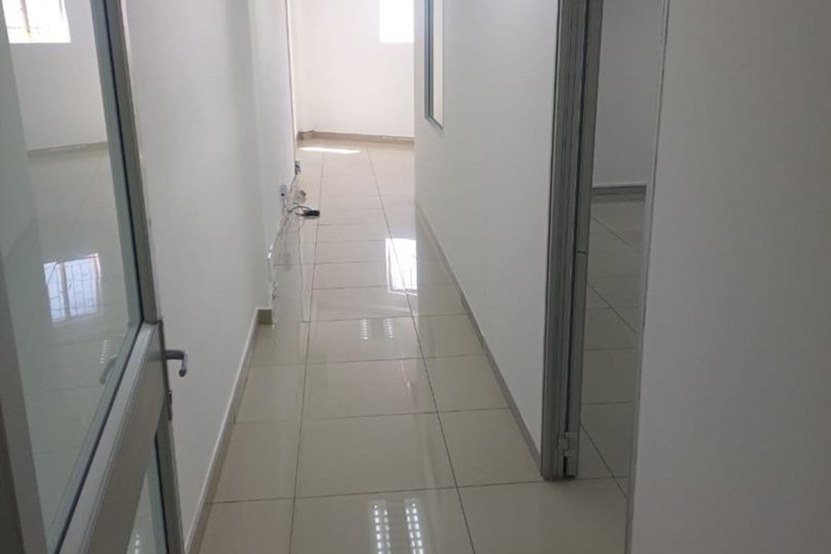 A clean, well-lit office hallway featuring polished tile flooring, suspended ceilings with recessed lighting, and modern aluminium-framed glass doors.