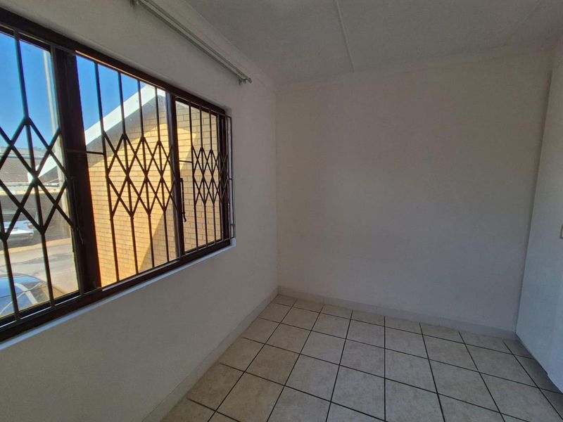 An empty bedroom featuring tiled flooring and a window fitted with a security gate.