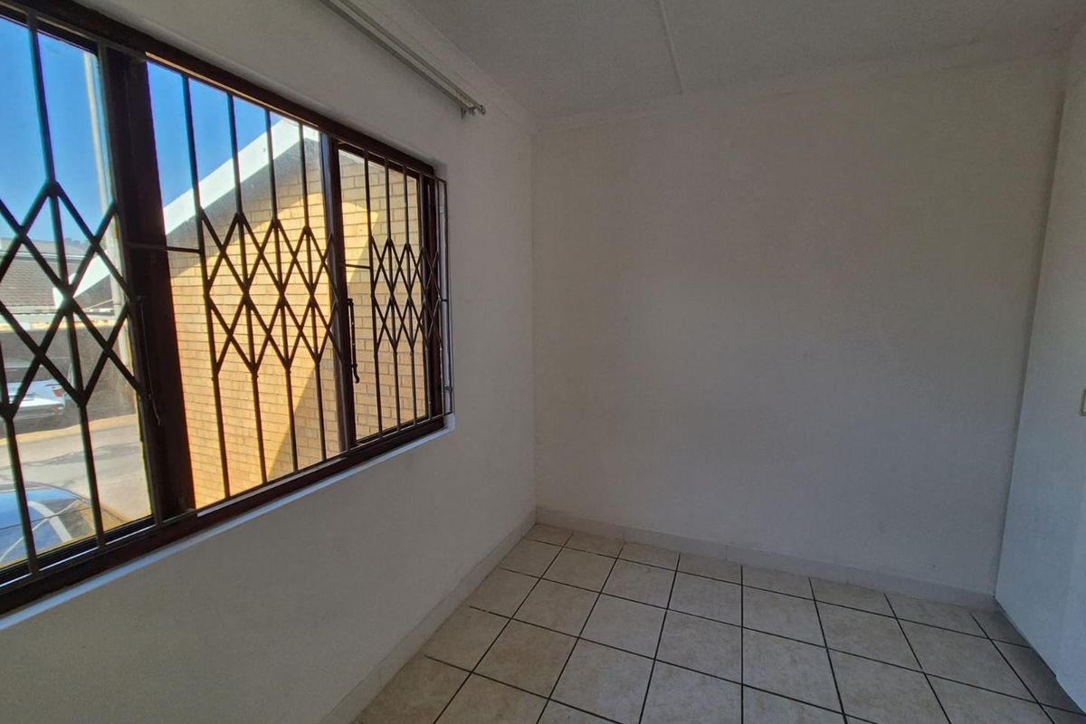 An empty bedroom featuring tiled flooring and a window fitted with a security gate.