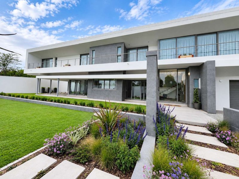 Modern two-story residence featuring stone cladding, expansive glass sliding doors, a spacious balcony with stainless steel railings, and a well-manicured garden.