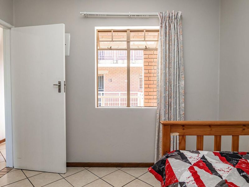 A functional bedroom featuring tiled flooring, a window with security bars, and neutral wall finishes, offering a clean and simple living space.