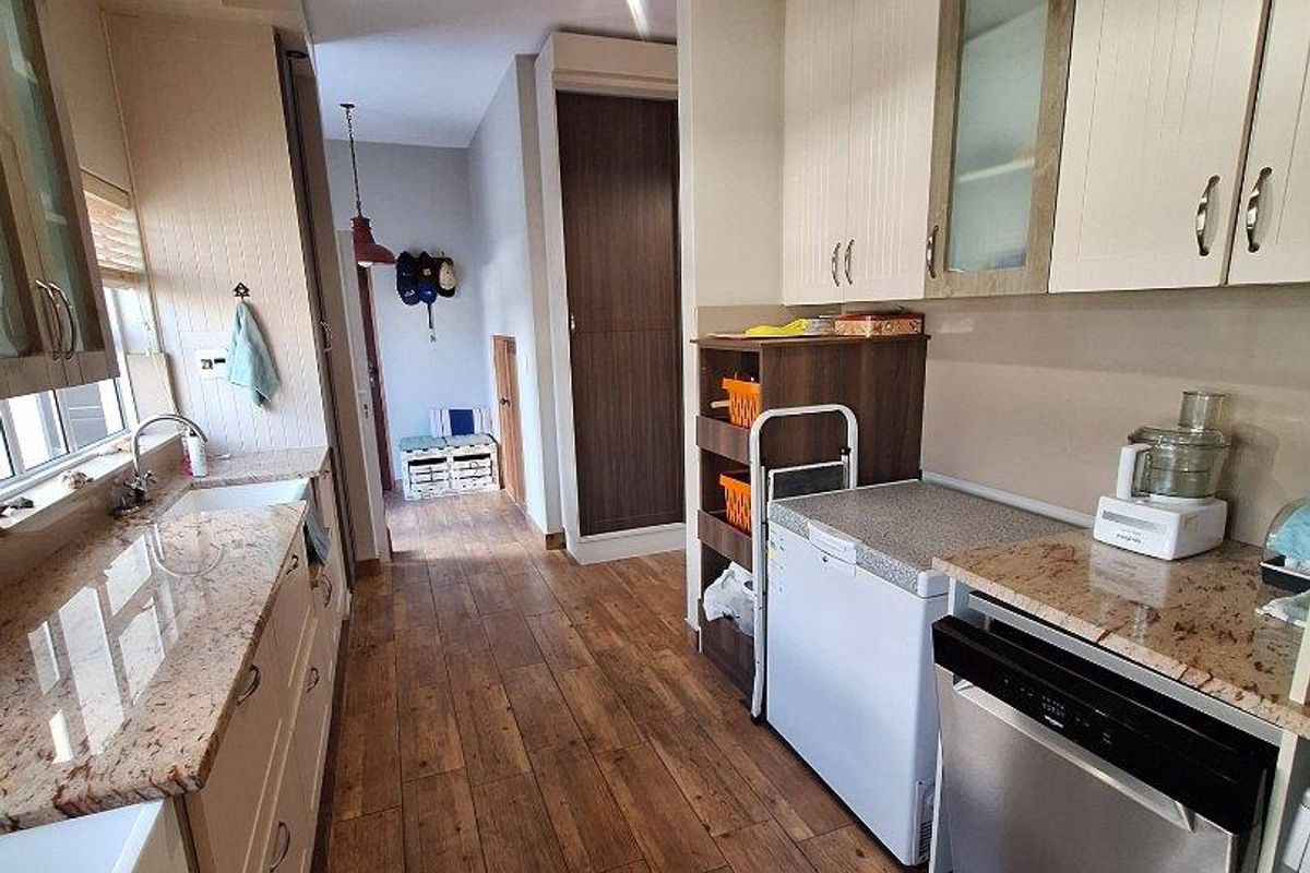 A functional kitchen featuring granite countertops, farmhouse-style sink, integrated cabinetry, and wood-look tile flooring, leading into a hallway area.