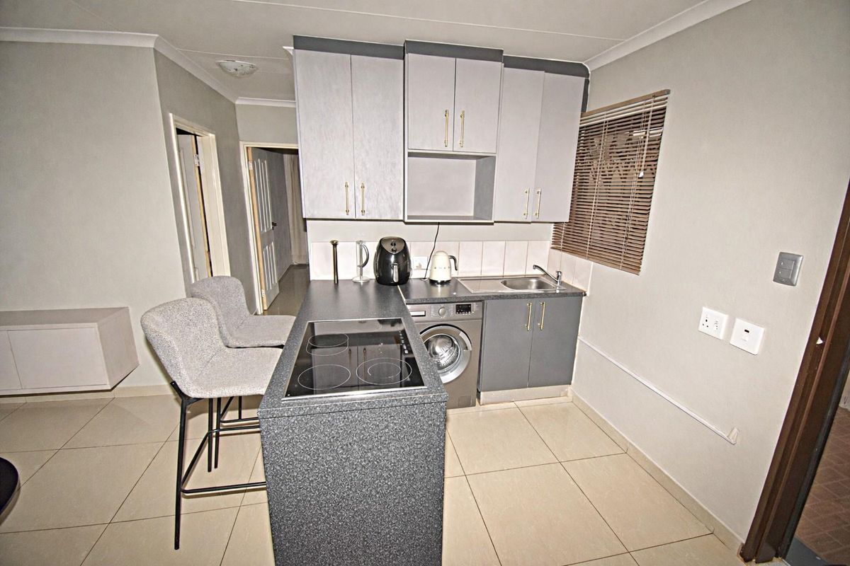 Compact kitchen featuring a breakfast bar with integrated electric hob, built-in cabinetry, stainless steel sink, and space for a washing machine.