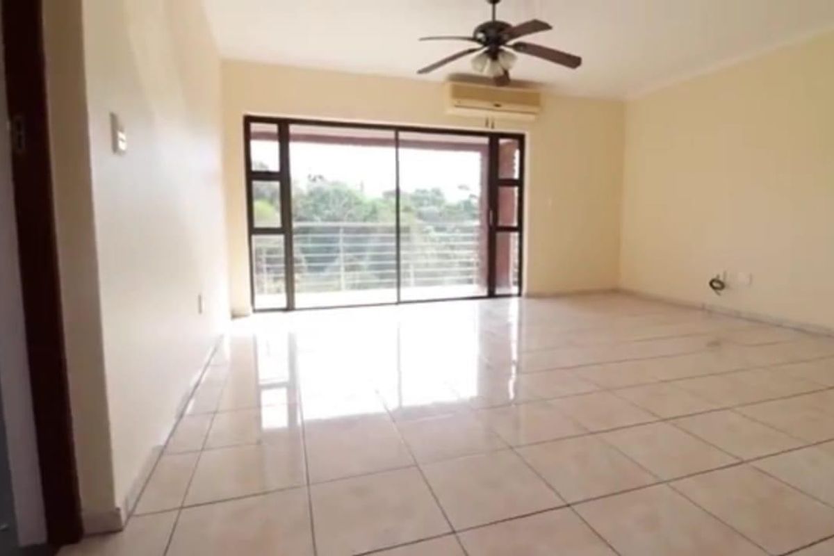 Spacious, empty living area featuring tiled flooring, a ceiling fan, wall-mounted air conditioning, and large sliding glass doors leading to an outdoor space.