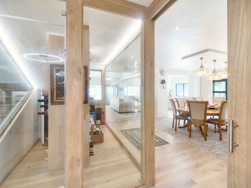 Modern open plan living area featuring a sophisticated glass-enclosed wine cellar, timber flooring, and elegant recessed lighting throughout the space.
