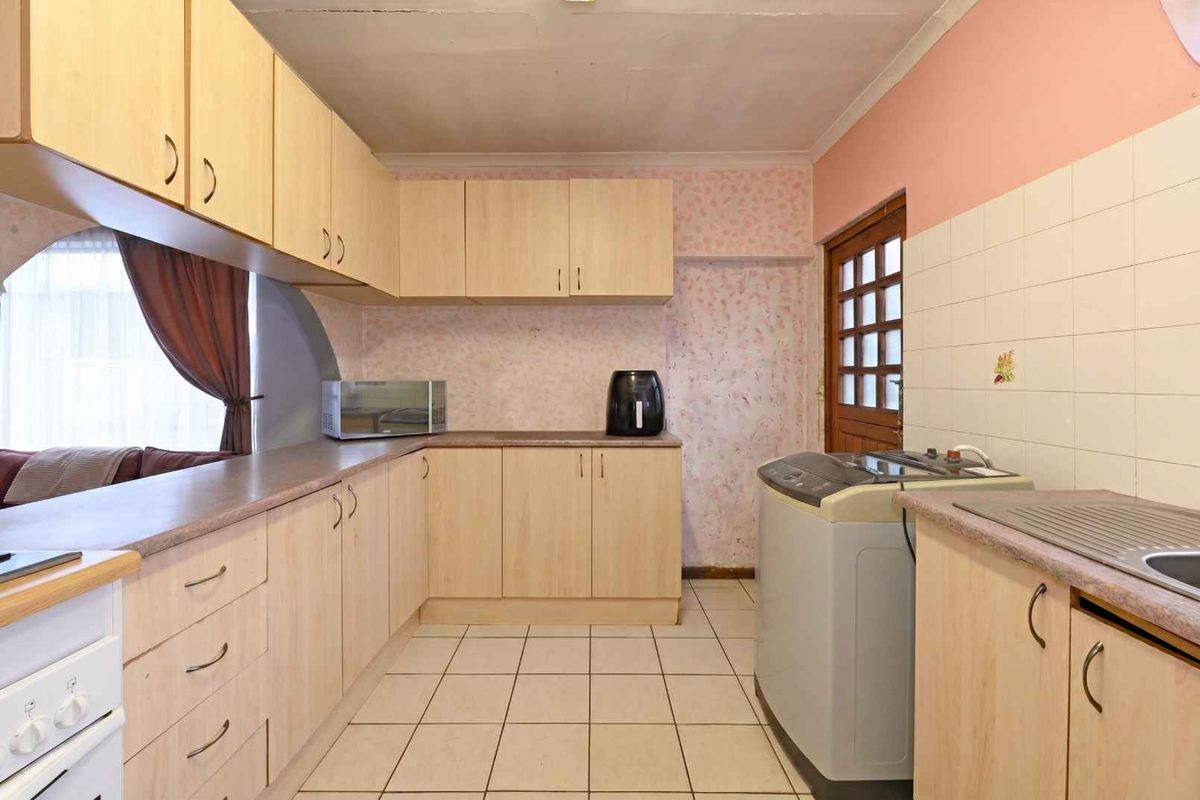 A functional kitchen featuring light wood-look cabinetry, tiled flooring, and a dedicated laundry area with direct access to the exterior.