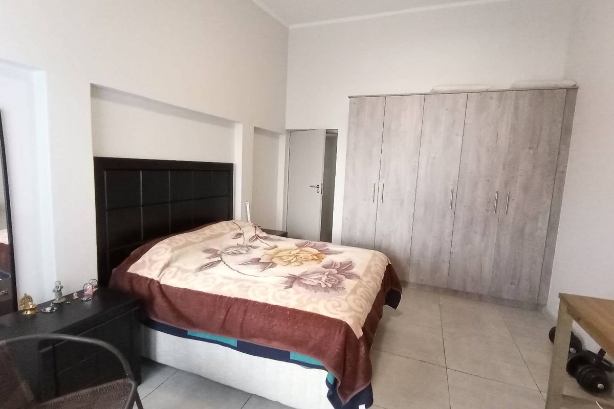 A spacious bedroom featuring large built-in wardrobes with a light wood finish and neutral floor tiling.