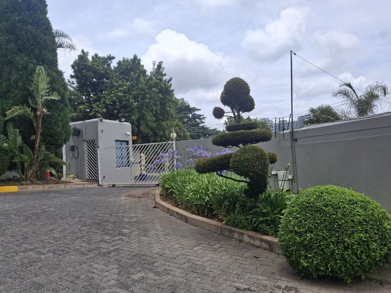 The property entrance features a secure gated access point, a guard house, and a well-maintained paved driveway with established landscaping and perimeter security.