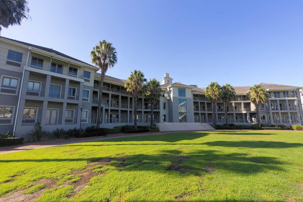 A wide-angle view of the office building exterior, featuring a multi-story facade with balconies and a well-maintained lawn in the foreground.