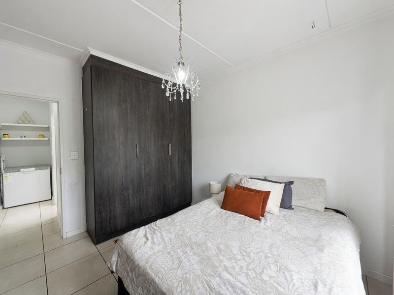 A well-maintained bedroom featuring a large dark wood built-in wardrobe, tiled flooring, and a decorative chandelier light fixture.