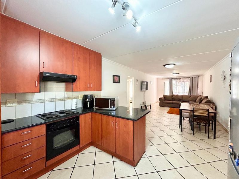 Open-plan living area featuring a kitchen with wood-finish cabinetry, granite countertops, and integrated appliances, flowing into a spacious dining and lounge area.