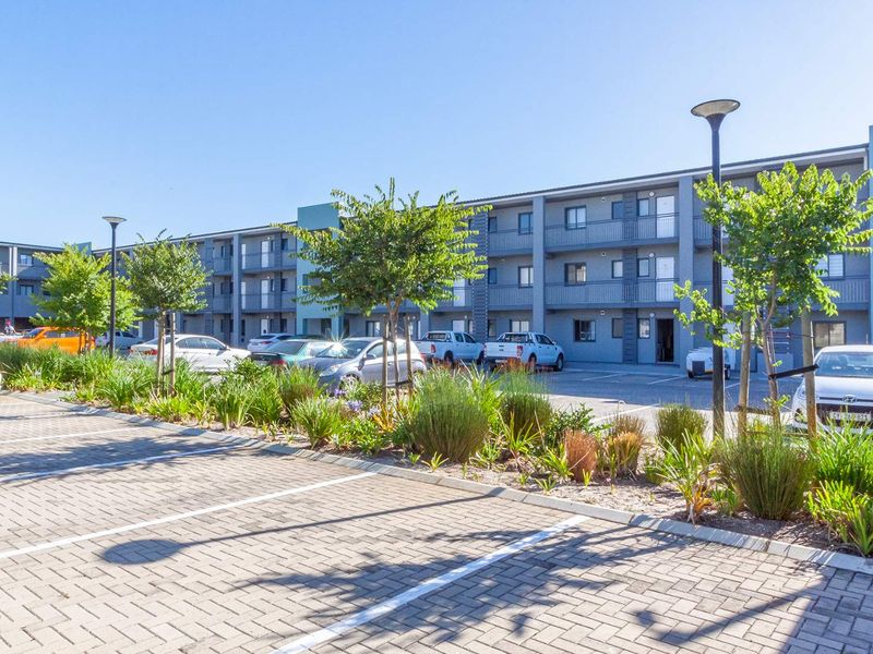 Exterior view of a modern multi-story apartment complex featuring a paved parking area and landscaped garden beds.