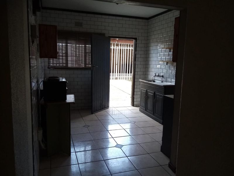 A dated kitchen featuring subway tile walls, tiled flooring, and a built-in sink unit with direct access to an exterior area.