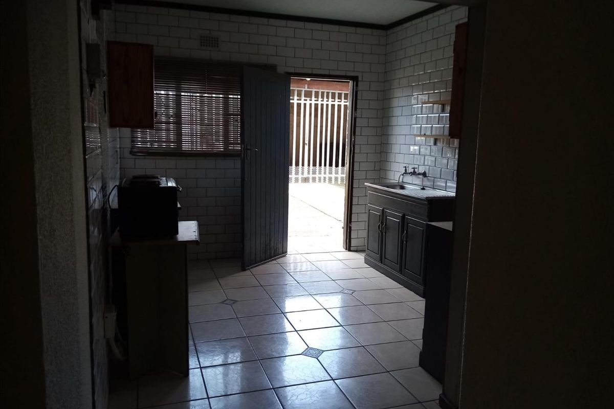 A dated kitchen featuring subway tile walls, tiled flooring, and a built-in sink unit with direct access to an exterior area.