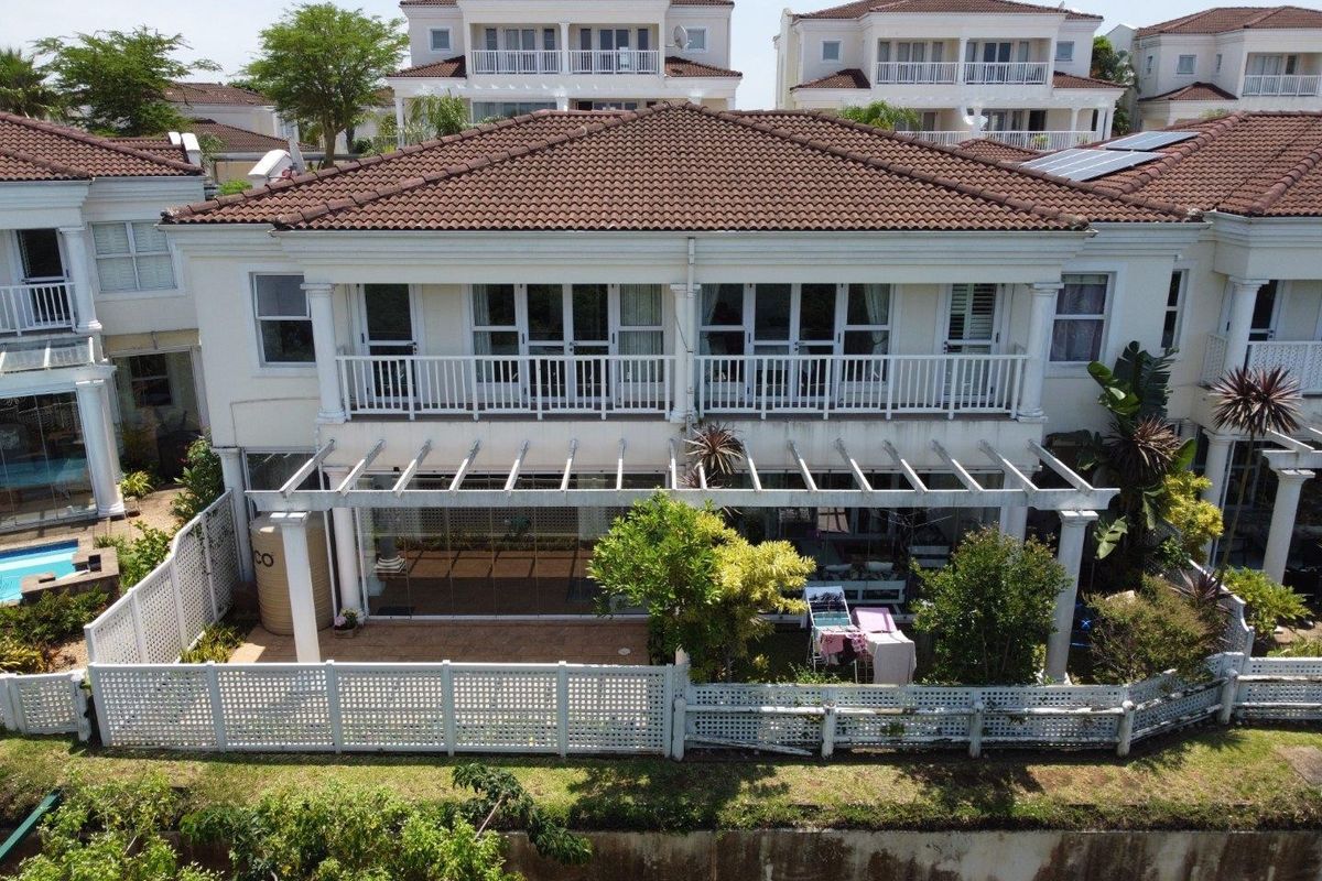 Aerial view of the rear elevation featuring a tiled roof, upper balcony, ground floor pergola, and enclosed patio area with sliding glass doors.