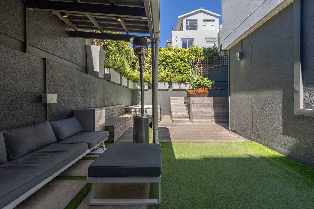 A private rear courtyard featuring timber decking, artificial lawn, built-in seating, and a pergola, creating a low-maintenance outdoor entertainment space.