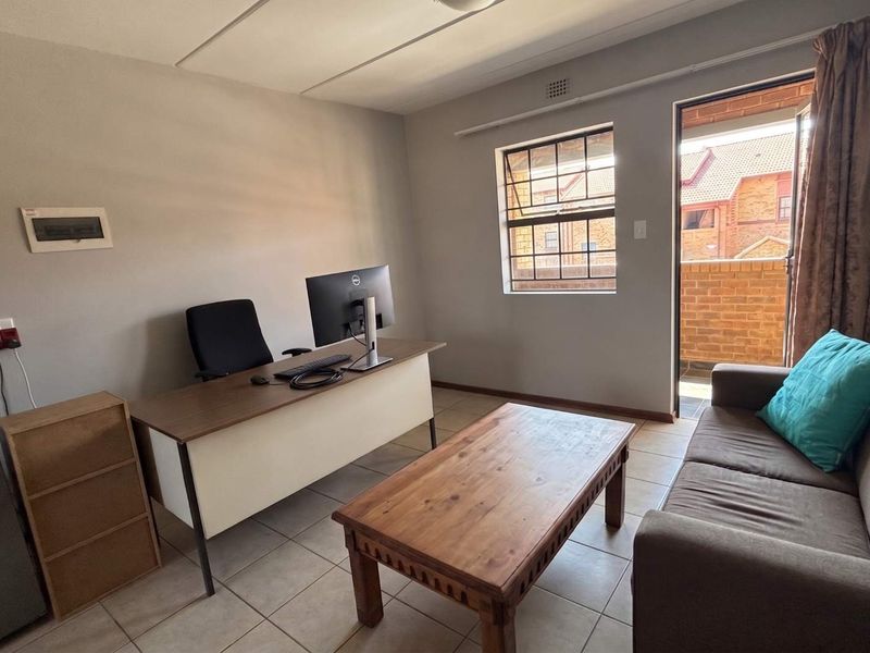 A functional living area featuring tiled flooring, a steel-framed window, and direct access to an outdoor balcony space.