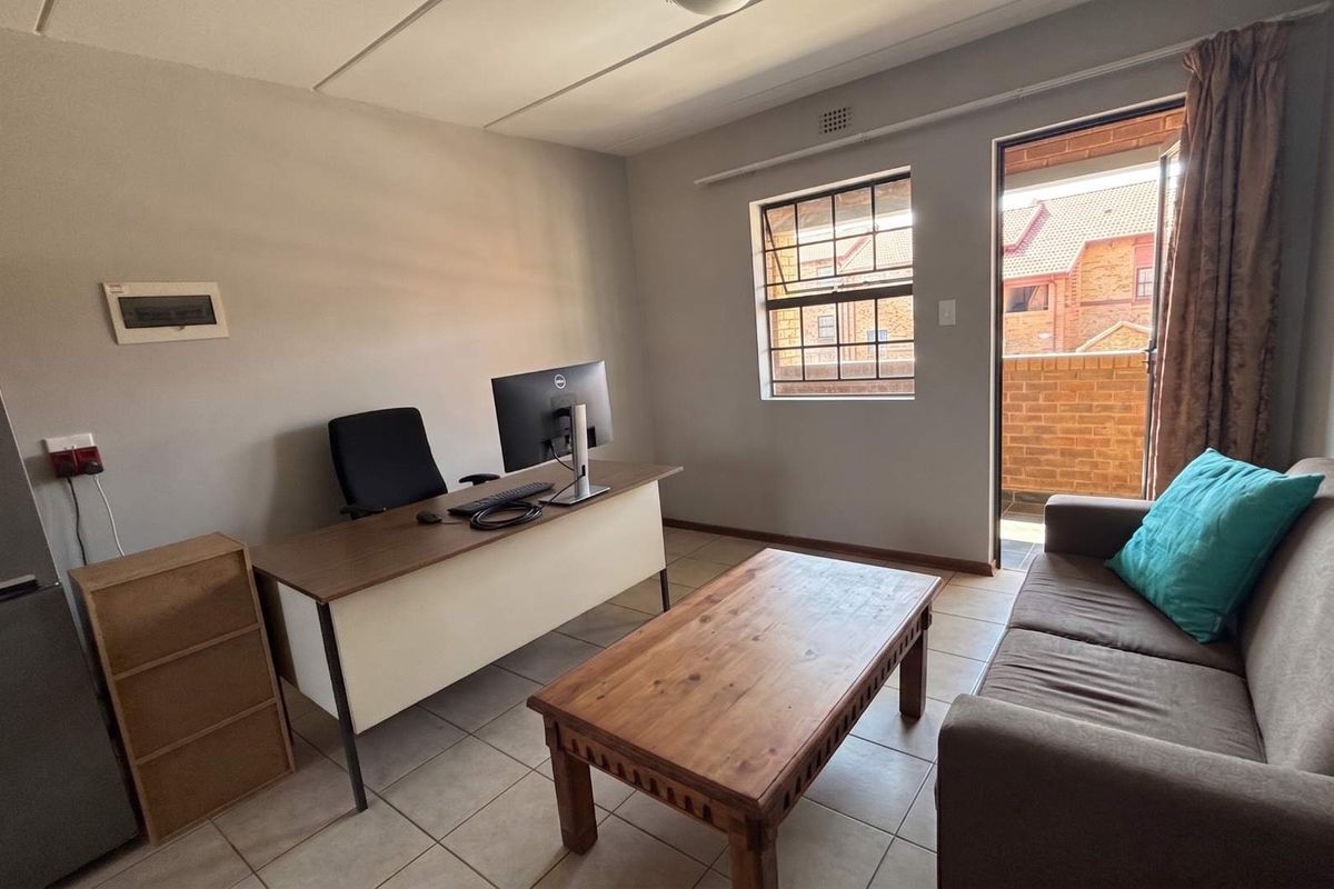 A functional living area featuring tiled flooring, a steel-framed window, and direct access to an outdoor balcony space.