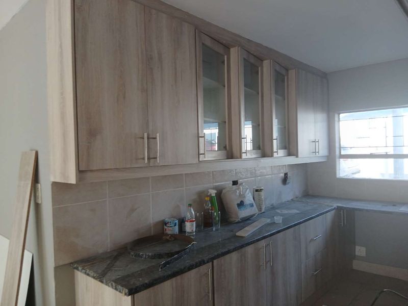 A functional kitchen featuring light wood-grain cabinetry, stone-look countertops, and a tiled backsplash, currently awaiting final finishing touches.