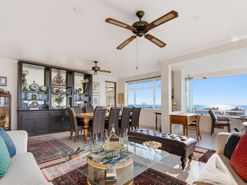 Spacious open-plan living and dining area featuring built-in cabinetry, ceiling fans, and expansive windows with panoramic ocean views.
