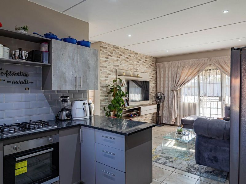 Modern open-plan living area featuring a well-appointed kitchen with granite countertops, gas hob, and a stylish stone veneer feature wall in the lounge.