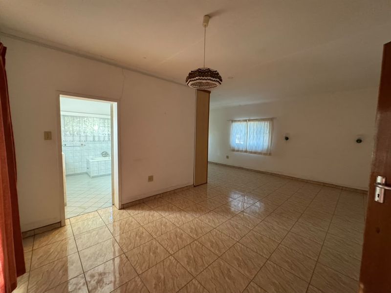 Spacious bedroom featuring tiled flooring, a built-in cupboard, and direct access to an en-suite bathroom, offering a blank canvas for renovation.