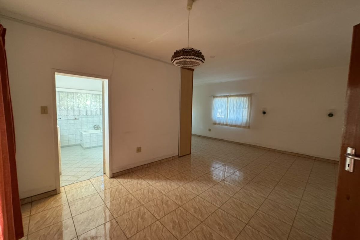 Spacious bedroom featuring tiled flooring, a built-in cupboard, and direct access to an en-suite bathroom, offering a blank canvas for renovation.