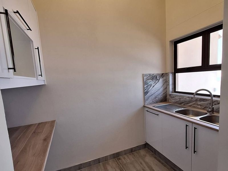 A clean, modern scullery featuring white cabinetry, wood-look countertops, a stainless steel sink, and stylish marble-look splashbacks with ample natural light.