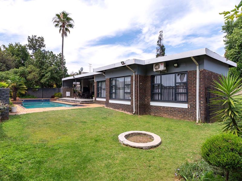 Rear view of the property featuring a brick facade, a swimming pool with paved surround, a covered patio area, and a landscaped garden.