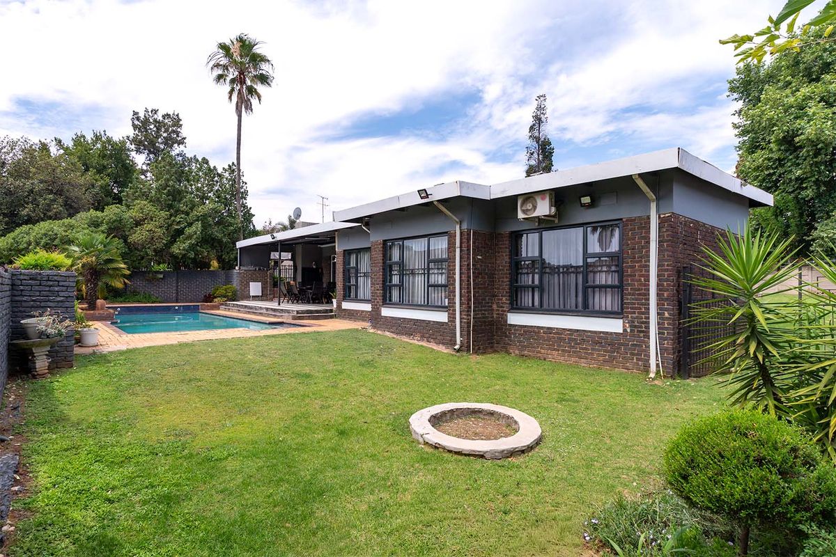Rear view of the property featuring a brick facade, a swimming pool with paved surround, a covered patio area, and a landscaped garden.