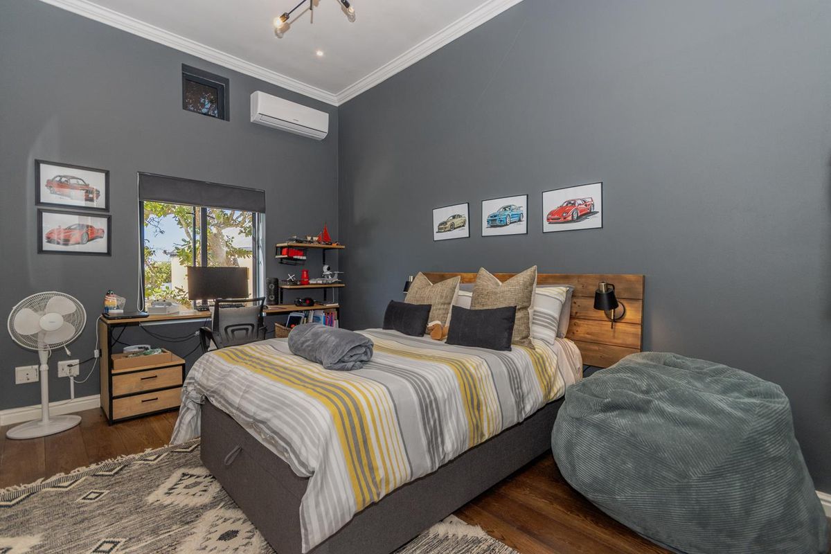 A well-maintained bedroom featuring dark grey walls, timber flooring, a split-system air conditioner, and a custom built-in headboard.