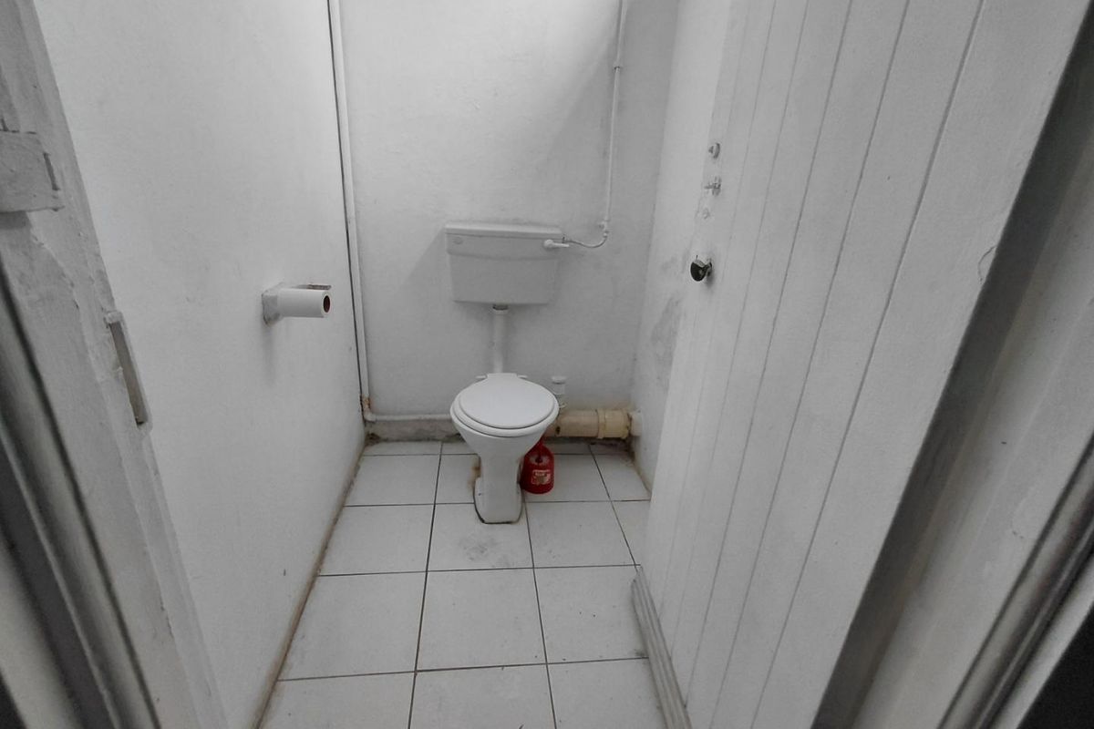A small, basic bathroom featuring a standard toilet and tiled flooring, requiring cosmetic updates and maintenance to improve its overall condition.