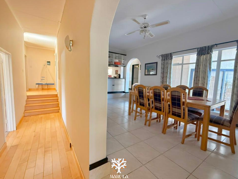 Open plan dining area featuring tiled floors, ceiling fan, and an arched transition to a hallway with hardwood flooring and built-in cabinetry.