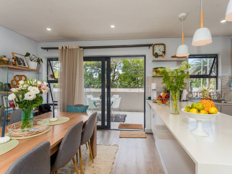 Modern open-plan kitchen and dining area featuring a stone-topped island, sleek cabinetry, and seamless access to a private balcony through sliding glass doors.