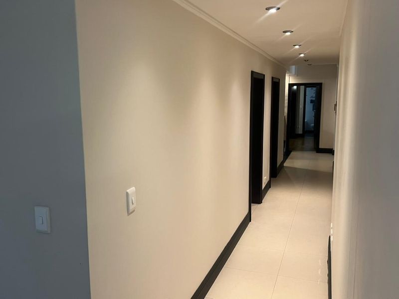 A clean, well-lit hallway featuring neutral tiled flooring, recessed ceiling downlights, and contrasting dark door frames.