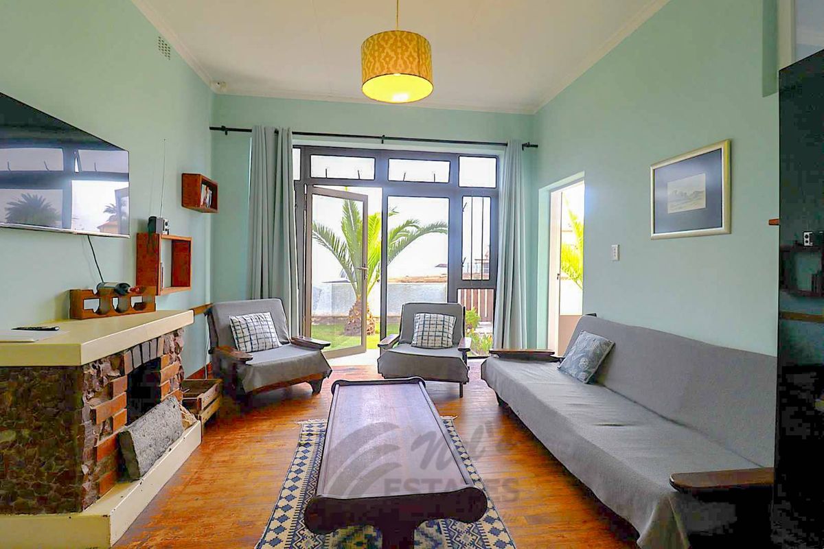 A cozy living room featuring a brick fireplace, timber flooring, and large glass doors providing direct access to the garden area.