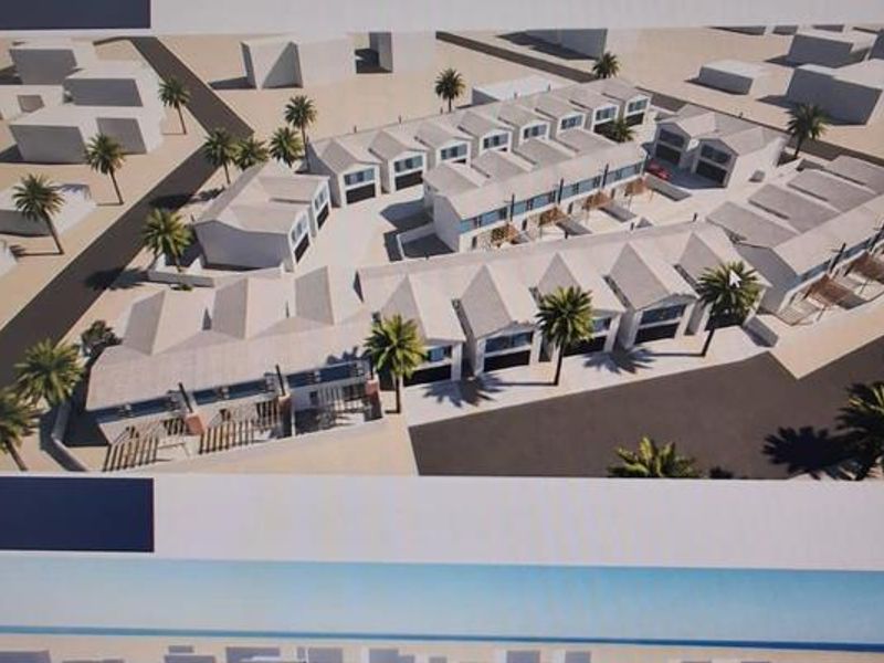 An aerial perspective rendering of a townhouse development complex featuring multiple residential units, paved access roads, and landscaped palm trees.