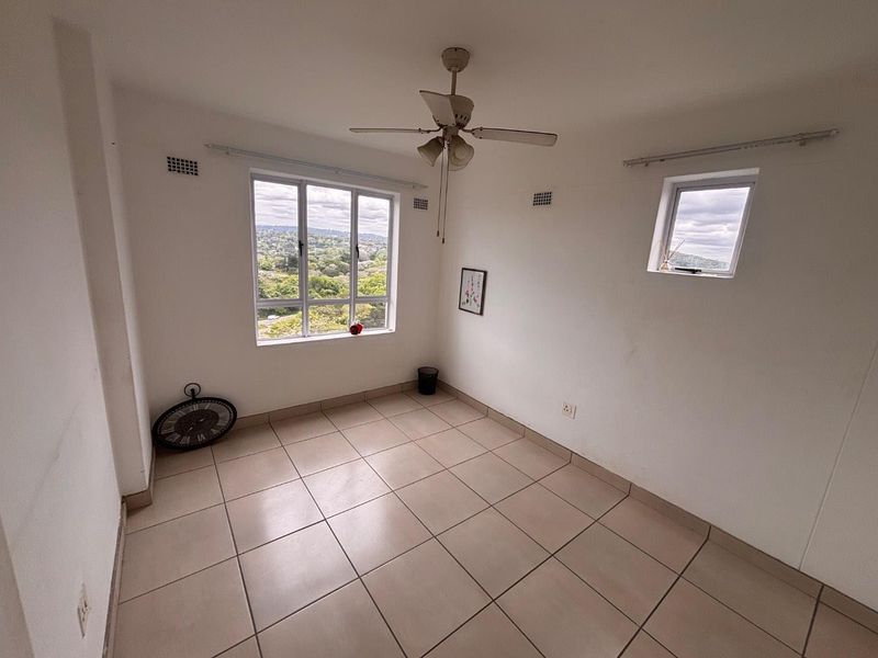 An empty bedroom featuring tiled flooring, a ceiling fan, and large windows offering scenic views.