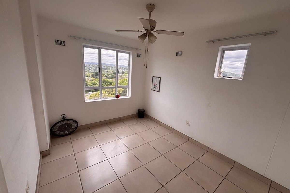 An empty bedroom featuring tiled flooring, a ceiling fan, and large windows offering scenic views.