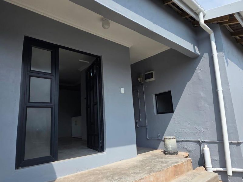 Rear exterior view of the apartment featuring a covered patio area, concrete steps, and modern black-framed glass door access.