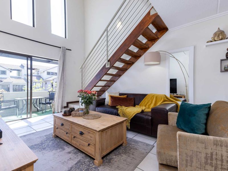 Spacious double-volume living area featuring a wooden staircase, tiled flooring, and large sliding glass doors leading to an outdoor balcony.