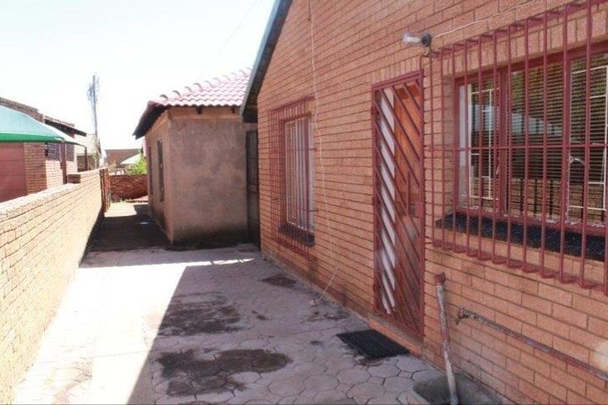 Side exterior view of the house featuring face brick walls, security bars on windows and doors, and paved walkway area.