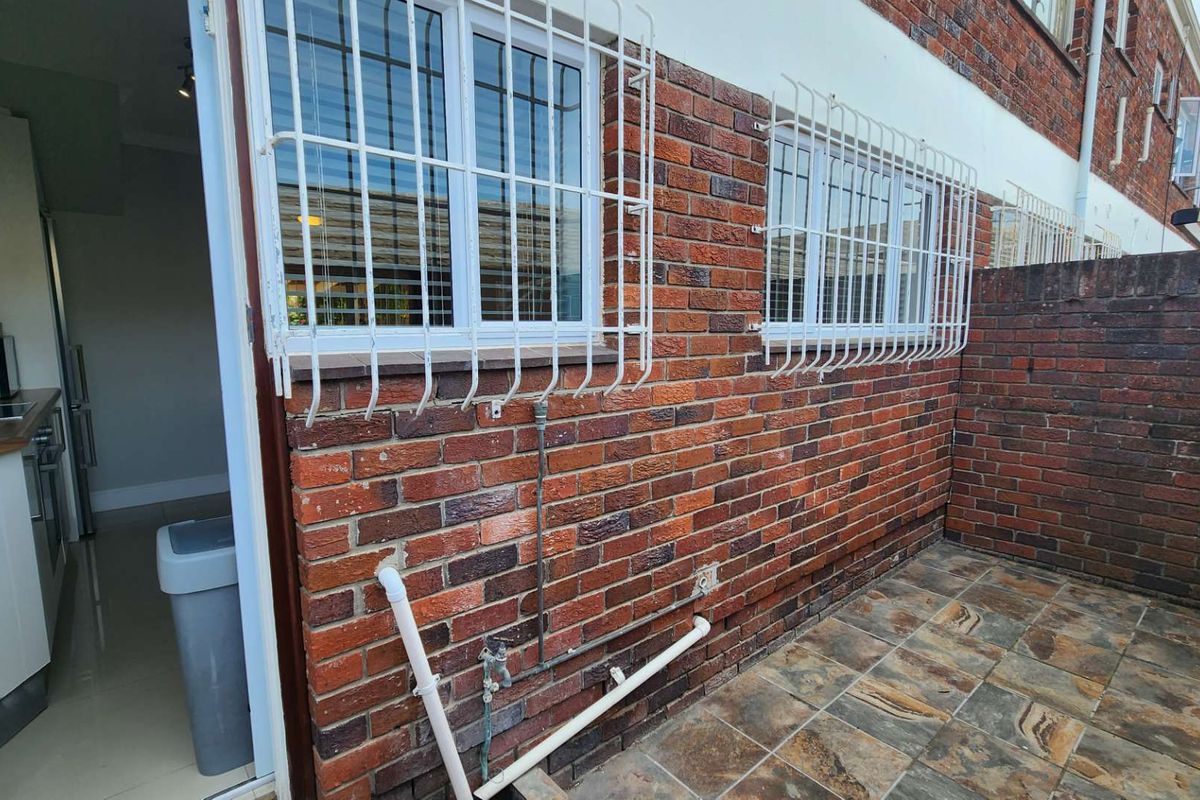 Rear exterior view of the townhouse featuring a tiled patio area, exposed brick facade, and security-fitted windows.