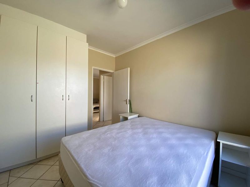 A functional bedroom featuring built-in cupboards, neutral wall tones, and tiled flooring, offering a clean and simple living space.
